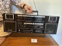 Front view showing entire Hitachi stereo with detachable speakers, control panel, cassette decks, and handle on top