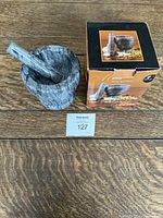 Grey marble mortar and pestle placed next to their original packaging box on a wooden surface.