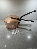 Full side angled view showing the copper pot with attached iron handle and lid, set on marble counter