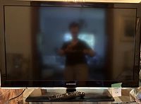 Samsung 42-inch TV front view powered off on glass swivel stand with remote on base.
