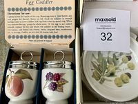 Photo showing two Royal Worcester egg coddlers in original box with usage instructions inside the lid, displaying fruit designs and metal lids with loop handles.