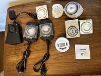 Top view of array of various plug-in electric timers, including black digital timers with cords and remotes, and white and beige mechanical dial timers.