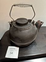 Closed view of the black cast iron kettle showing the spring handle and spout with some rust.