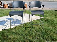 Two high black plastic and metal bar chairs placed on a lawn with armrests and footrests. Chairs show signs of repairs.