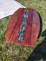 Oval coffee table showing wood surface with central tile inlay on grass outdoors