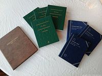 Eight coin albums arranged on white surface showing green U.S. Coins albums and blue Lincoln Wheat Penny sets with additional brown Mercury Dimes album.