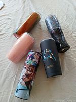 Six custom tumblers laid horizontally showing diverse designs and colors, including glitter and artwork.