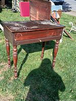 Vintage wooden writing desk with four turned legs, hinged top open showing storage inside, visible scratches and damage.