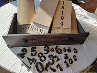 Set of three wooden home signs stacked inside a wooden drawer with black metal numbers scattered in front, showing the '18104' number on one of the signs.