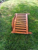 Single wooden kids bed frame laid on grass showing side rail with carved leaf design and wooden slats