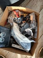 Open box showing various vintage knobs mostly metal and glass, some with decorative crystal styles packed loosely and in small plastic bags