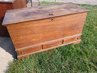 Heavy large vintage wooden chest outdoors on grass, showing full front and top with visible key lock and scratches on surface.