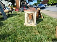Wooden side table with glass door and light visible inside on grass outdoors