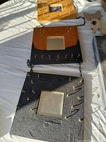 Three-piece black and brown wall hanging with gold hooks and small square mirrors, linked by chains