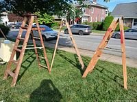 Three wooden painter's ladders standing on grass outside, angled to show condition and structure.