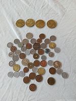 Photo showing a collection of approximately 40 mostly round coins and tokens in various sizes, colors and conditions spread on white background.