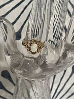 Ring displayed on clear hand display showing top view of opal and filigree design