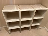 Three identical narrow white shelving units with two shelves each lined up side by side against a wall.