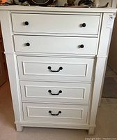 Front-facing image of a white contemporary dresser showing five drawers with mixed black round and decorative pull handles.