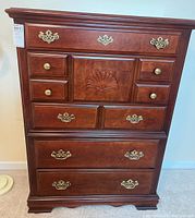 Front view of wooden highboy dresser showing carved shell design and brass handles.