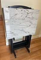 Three faux marble tray tables stacked in a black stand, showing the front surface and handle cutout