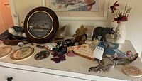 Top view of assorted figurines and decorative items on a white surface including framed art, plaques, and animals figurines.