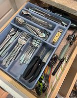 Four kitchen drawers containing flatware and various kitchen utensils organized in plastic trays.