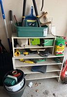 Photo of shelf with gardening tools including green trays, plant food container, and various hand tools