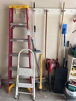 Photo of ladders and yard tools lined up against wall in garage.