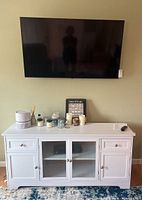 Front view of the LG 56 inch LED Smart TV mounted on a wall above a white cabinet showing its size and reflective screen.