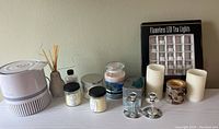 Photo showing multiple candles including flameless LED tea lights set, jars of candles, candle holders, reed diffuser, and a white appliance on table.
