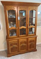 Full front view of oak hutch with three glass doors and three wood doors below, showcasing decorative floral carvings and ring pulls.