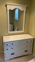 Photo of entire painted white wooden dresser with attached mirror, showing floral detailing and multiple drawers.