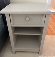 Frontal view of one bedside table showing drawer, knob, open shelf, and legs.