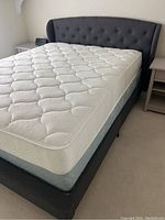 Full assembled queen-size bed including gray upholstered headboard, box spring and white mattress