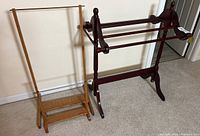 Natural wood quilt rack and dark cherry finish quilt rack side by side against wall on carpeted floor
