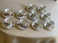 Photo of all 10 teacups and saucers showing the various patterns including gold trim, English Roses, Clare pink-blue florals, and Queen Anne purple florals.