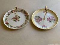 Top view of two Old Foley dessert plates with floral patterns. Each plate features a gold-tone handle in the center for carrying.