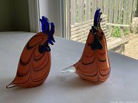 Front view of two glass rooster figurines showing detailed blue combs and orange swirl patterns.