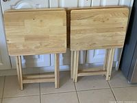 Four wooden folding table trays standing upright against kitchen cabinet.
