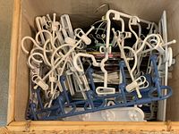 Top view of a basket containing various specialty clothes hangers including white plastic hangers with clips, and a blue hanger with multiple pegs, showing the varied shapes and designs.