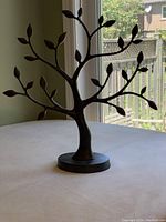 Front angled view of the metal tree sculpture showing branches and leaves with round base