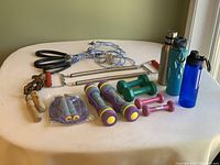 Full lot showing exercise ropes, dumbbells, skipping ropes, metal spring chest pull exerciser, and water bottles.