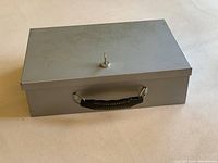 Closed heavy steel fire safe lockbox with key slot and black handle pictured from above.