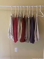 Nine pairs of pants hanging on a rail, showing the range of colors including beige, red, brown, and purple.