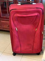 Red large suitcase front view showing fabric body with front zippered pocket and some scuffs.