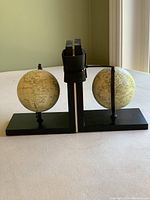 Pair of black globe bookends with rectangular bases on a light surface against a pale green wall.