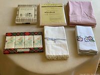 Showing entire lot including box of manicure and brush set, packaged pillowcases, four decorative napkins with floral designs, and additional pillowcases in pink and white fabrics.