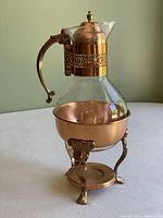 Close-up side view of the copper and glass coffee/tea carafe placed on a surface with plain background.