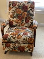 Front view of a wooden rocking chair upholstered with a fall-colored floral pattern fabric, showing the full chair including padded seat, back, and armrests.
